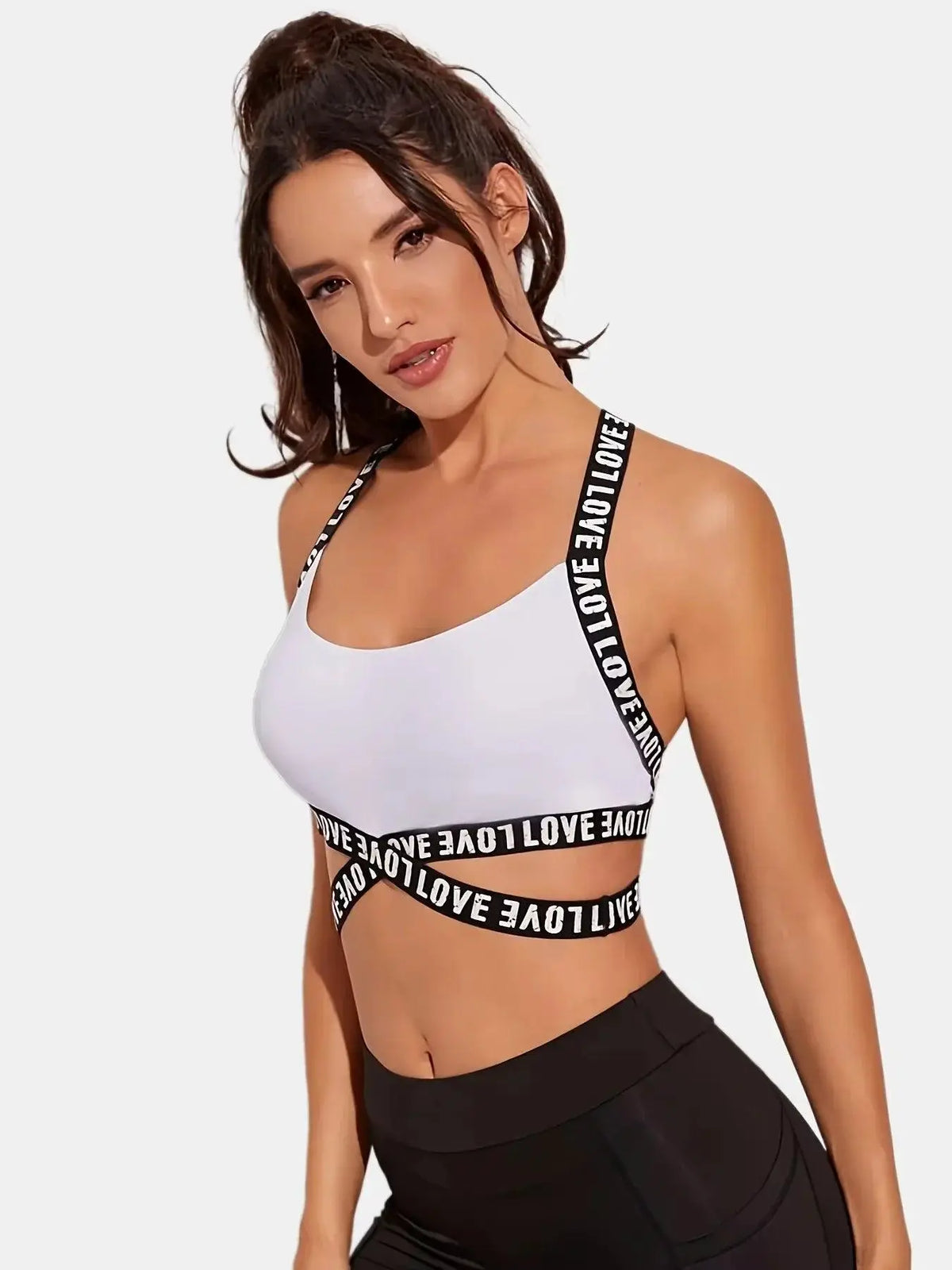 Woman modeling white sports bra with black 'LOVE' straps, black leggings, on white background, OurLum.com